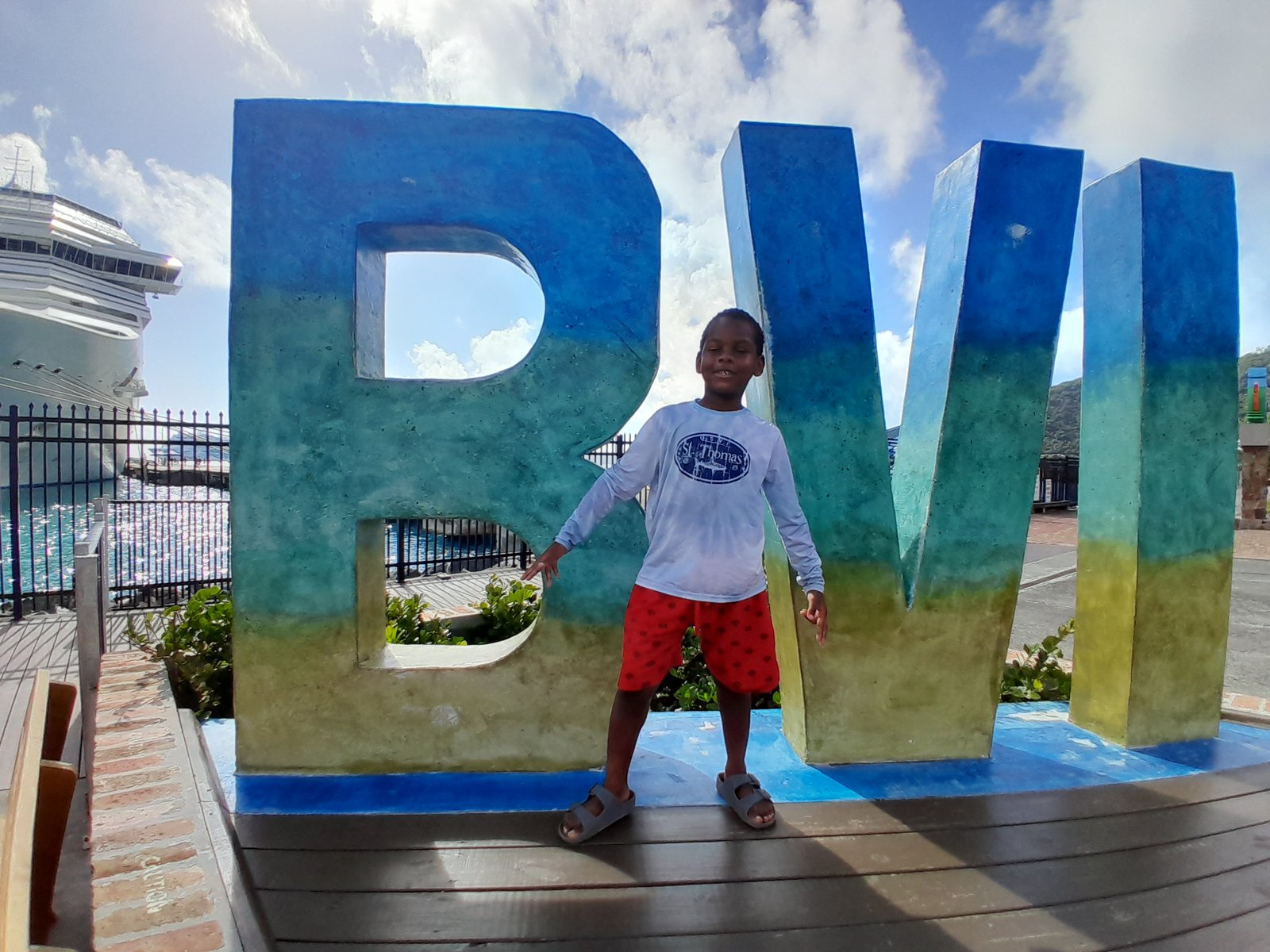 A young boy in a white long-sleeve shirt and red shorts stands posing in front of a large, colorful 